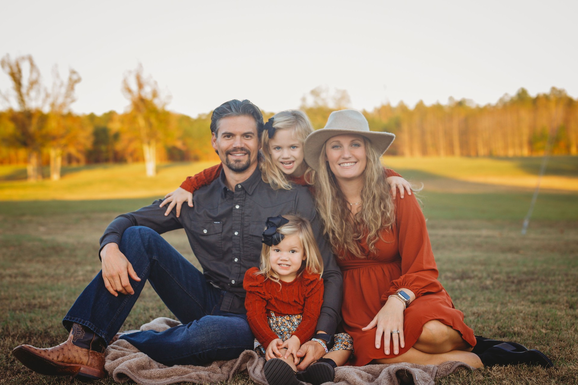 Sean and Ashley with their two daughters in a golden field at sunset in Delight Arkansas