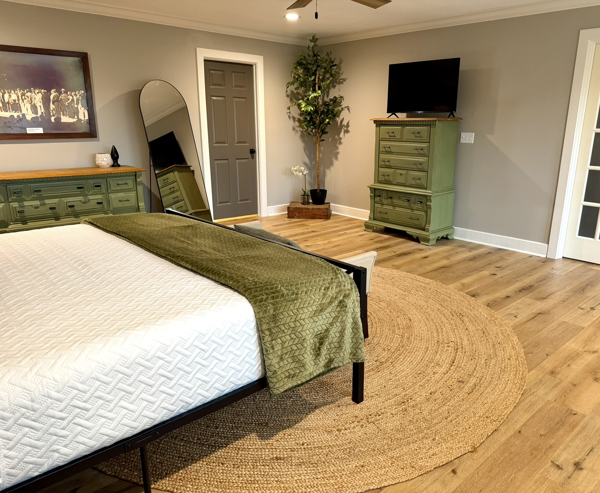 Primary suite king bed with olive green bedding and distressed green dresser