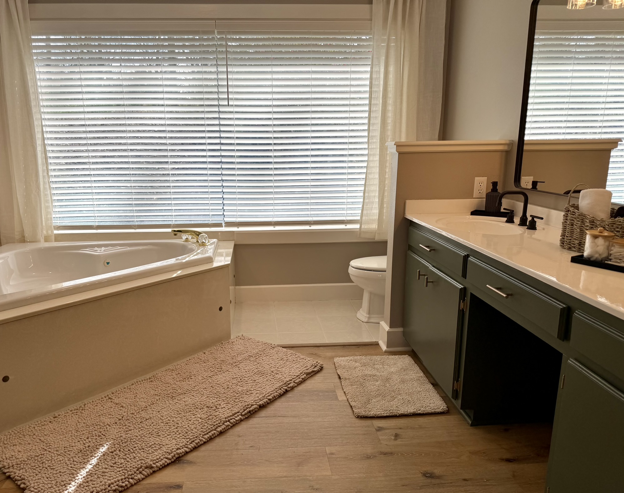 Primary bathroom wide view with jetted tub green vanity and wood floors