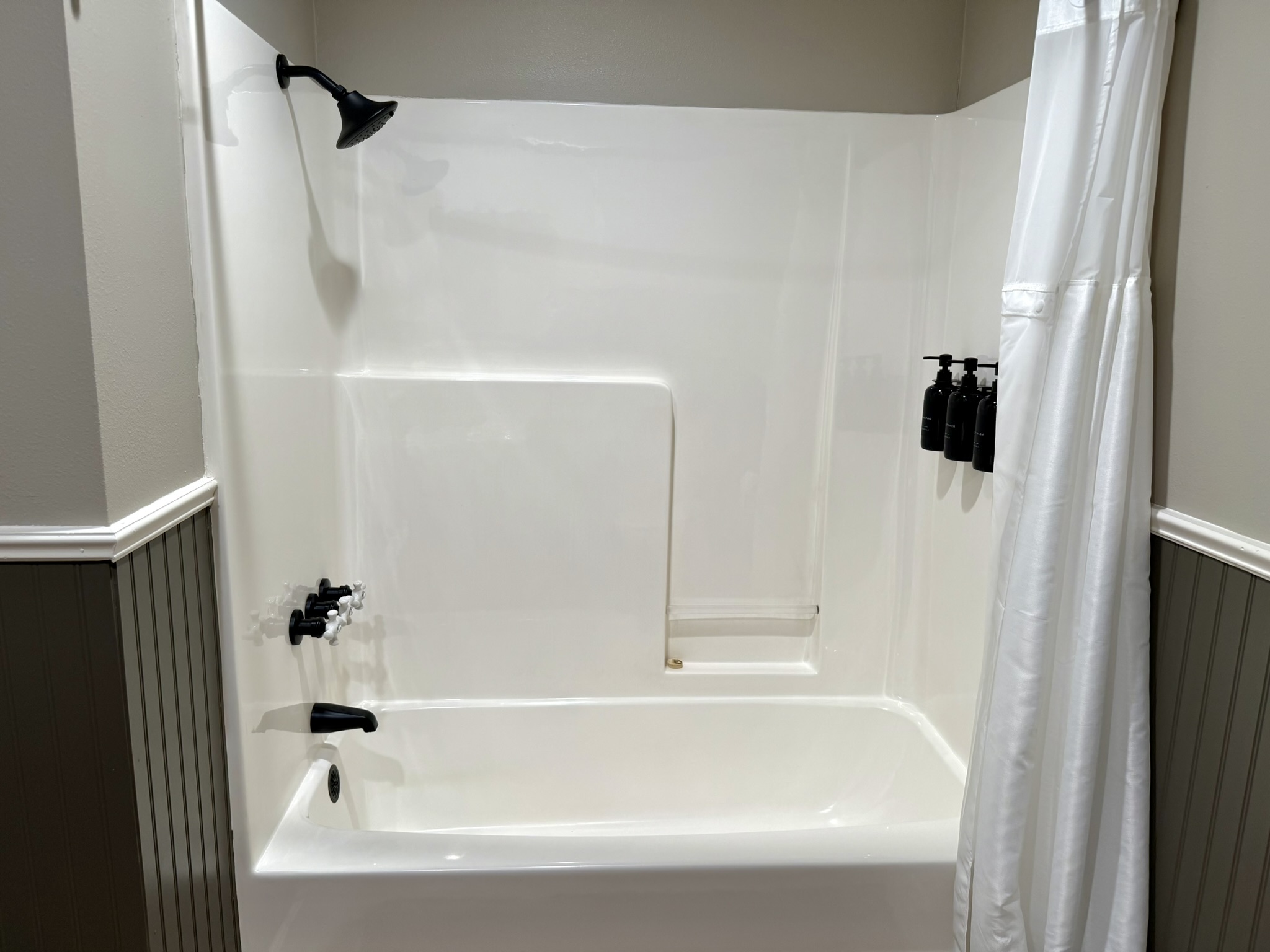 Third bathroom tub shower combo with beadboard walls and shampoo dispensers