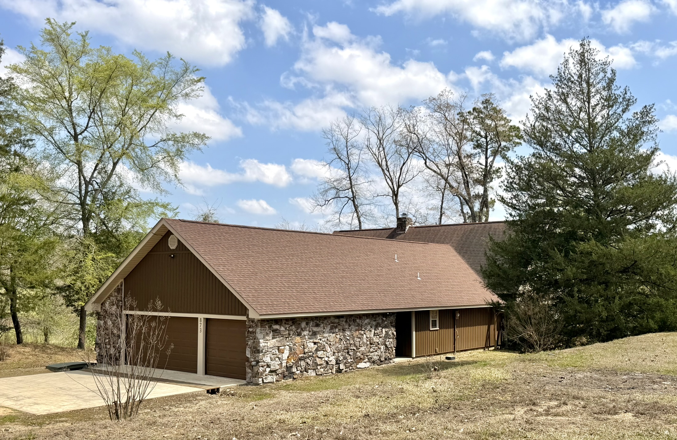 Southern Delight front view with A-frame garage stone facade and tree-lined property