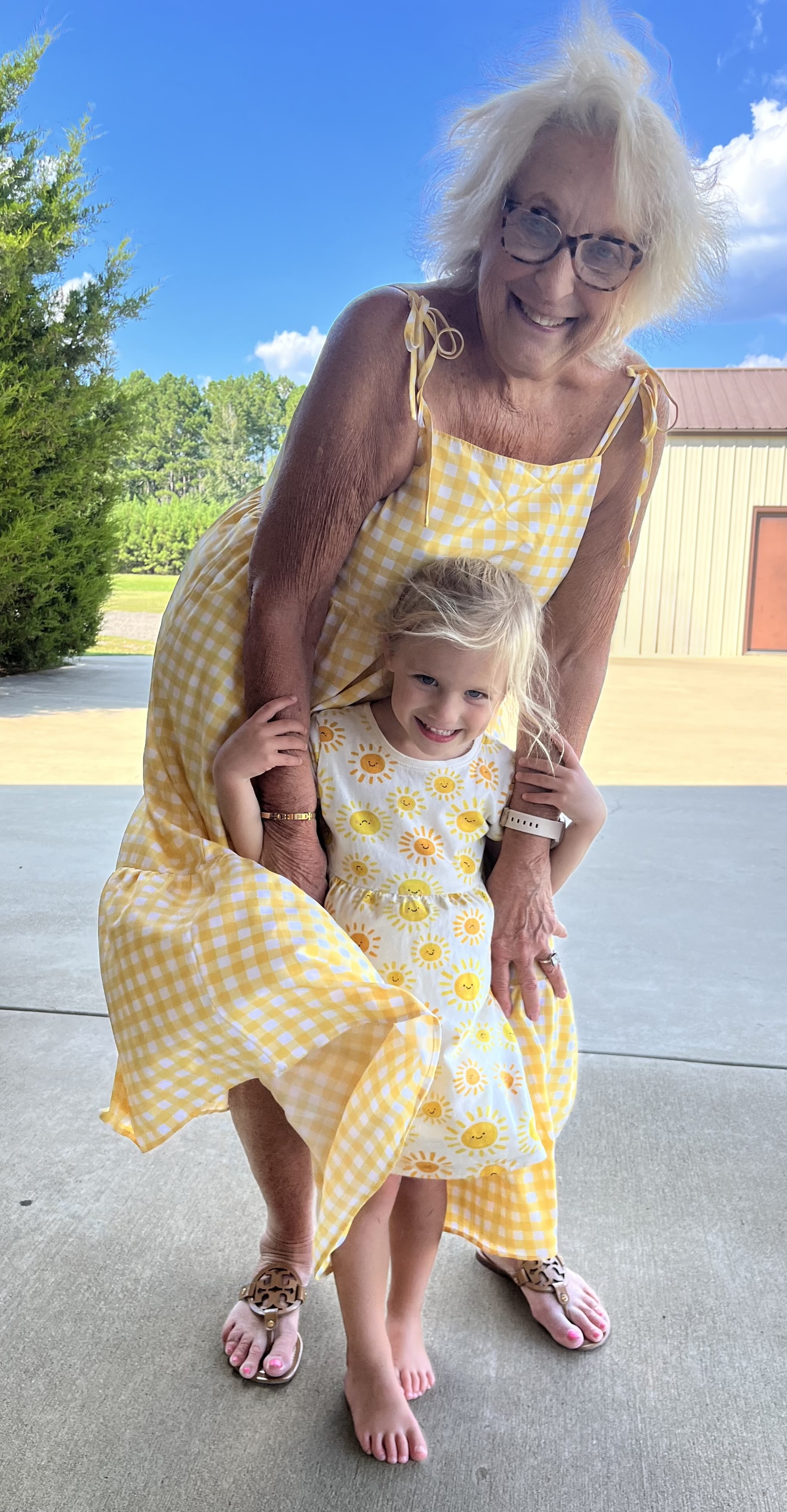 Nawnee hugging her great-granddaughter in matching yellow dresses on a sunny day